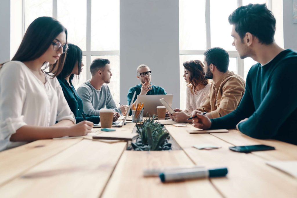 La riunione del personale di un'azienda, incarnata da un gruppo di giovani in abbigliamento smart casual, che discute dell'ordine del giorno all'interno di un ufficio alla moda